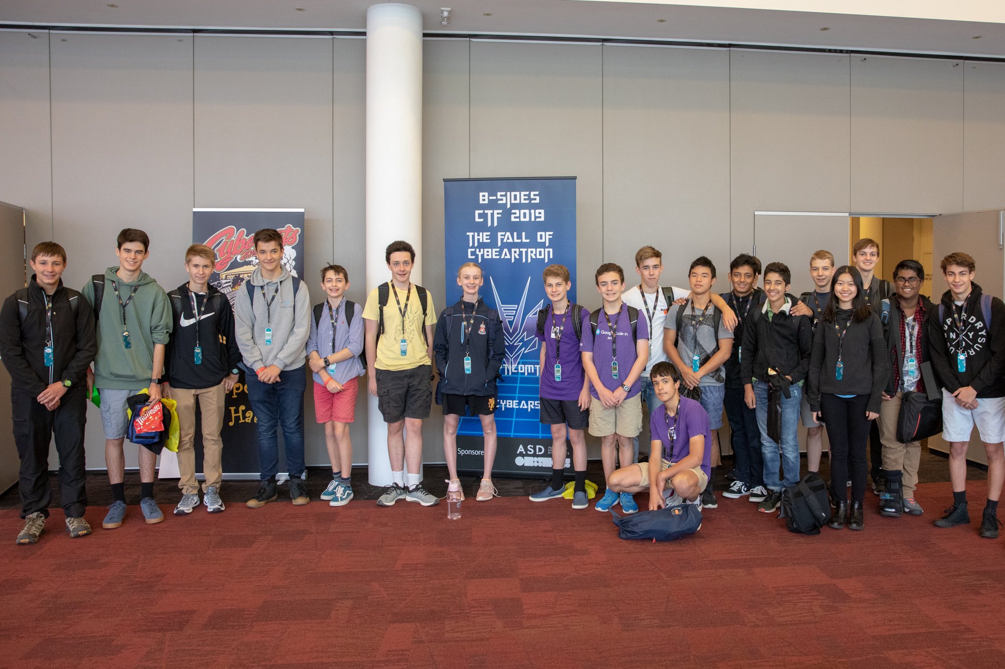 Students pose for a photo in front of a banner that reads 'BSides CTF 2019 - The fall of Cybeartron'.